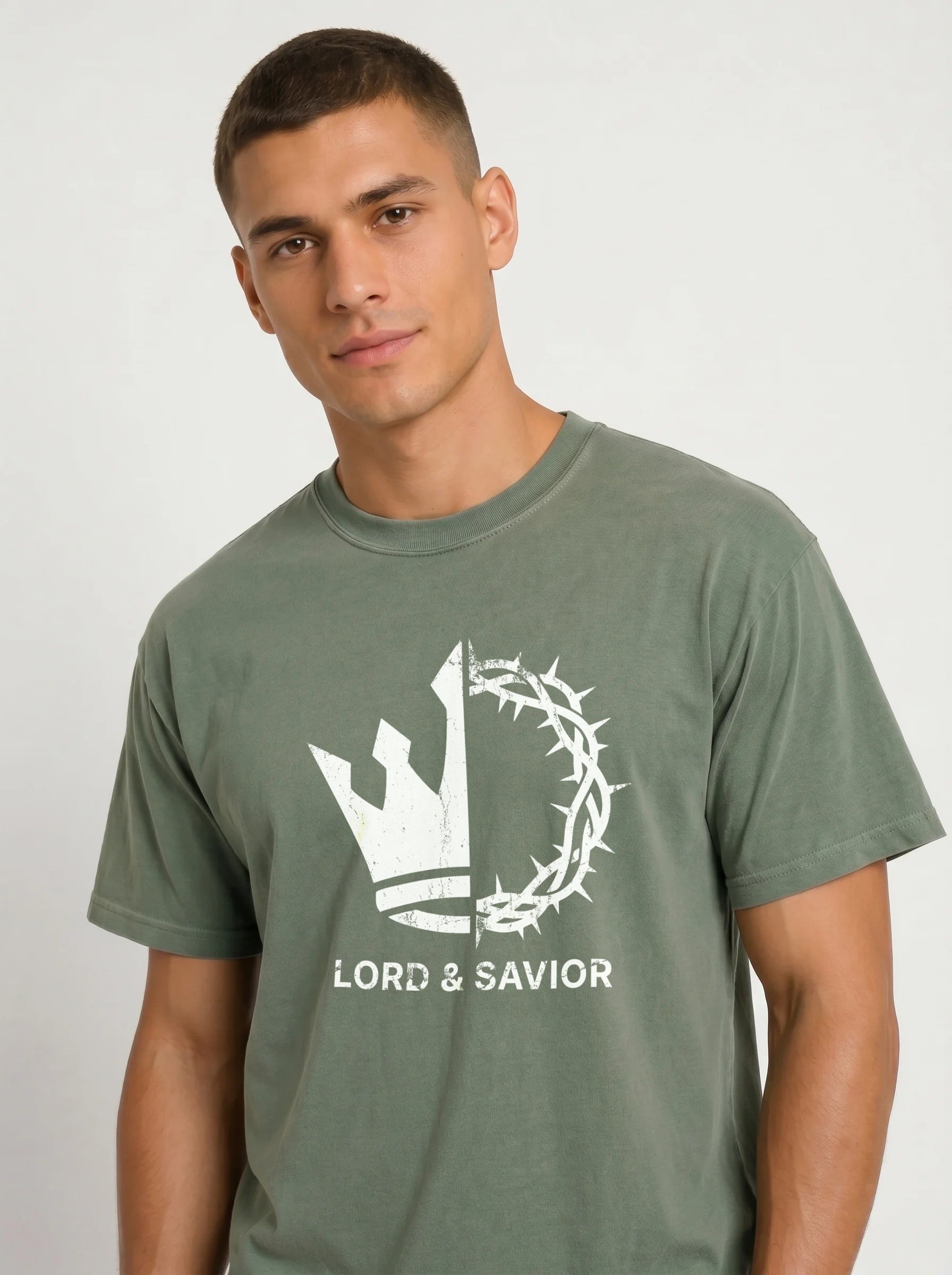 A man wearing an olive green t-shirt with a white graphic of a crown of thorns and a cross, with the text 'LORD & SAVIOR' printed below, against a light gray background.