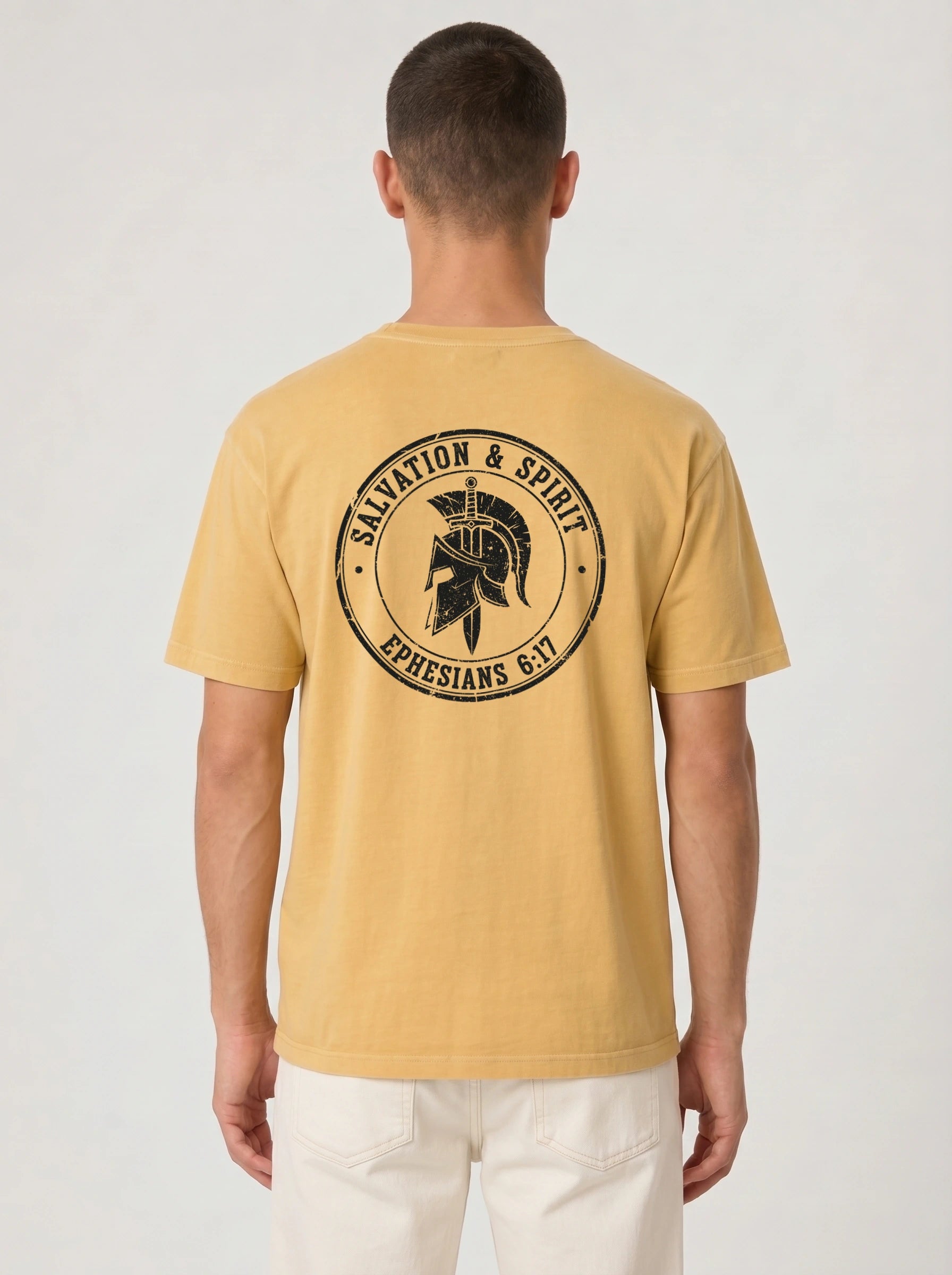 A man viewed from behind wearing a mustard yellow t-shirt with a black circular graphic on the back featuring a Spartan helmet and the text 'SALVATION & SPIRIT EPHESIANS 6:17'.