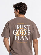 Person shown from behind wearing a faded brown T-shirt with a large “JEREMIAH 29:11” and “TRUST GOD’S PLAN” design with the verse below.