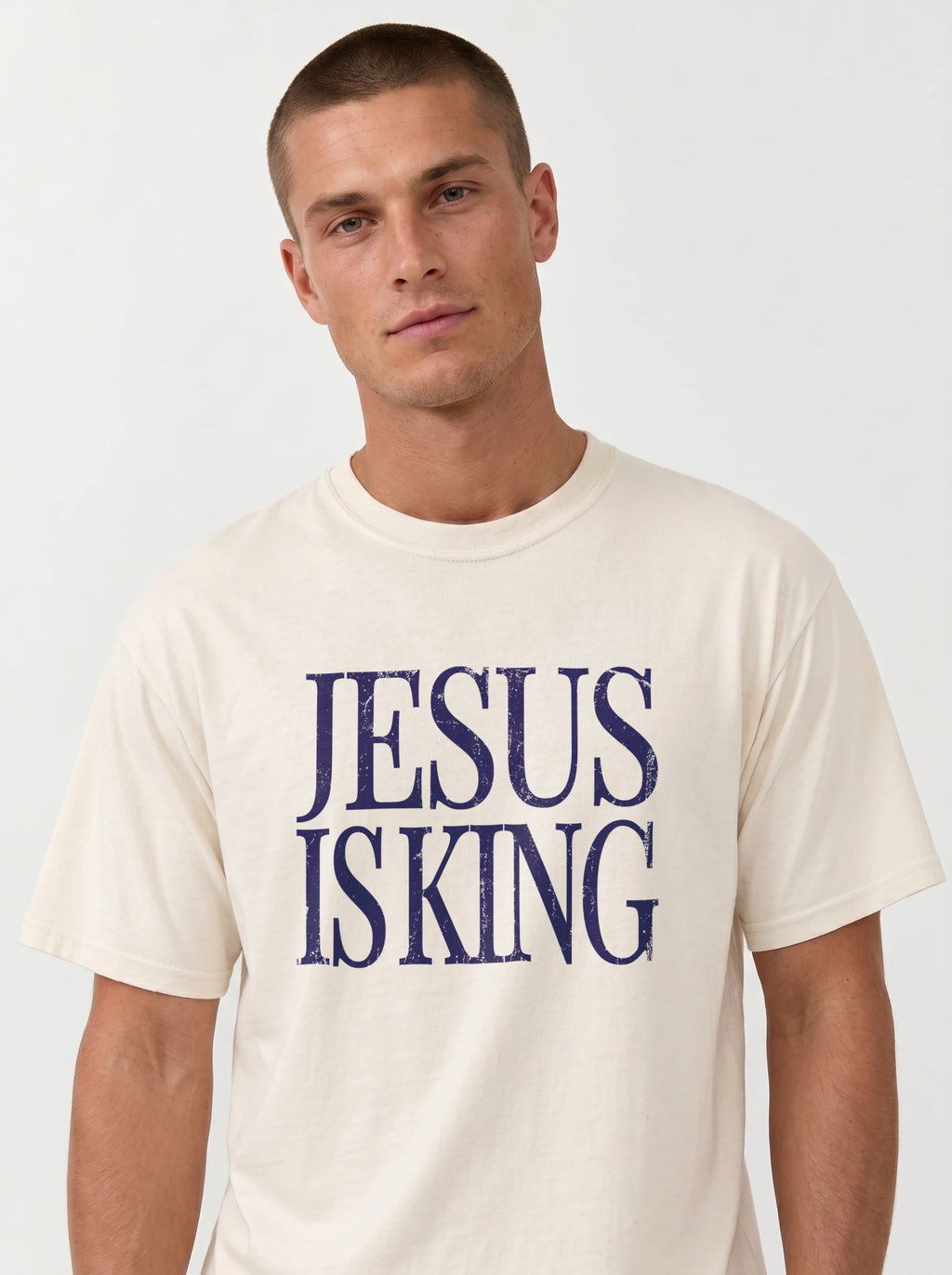 Person wearing a cream T-shirt with distressed navy text reading “Jesus Is King.”
