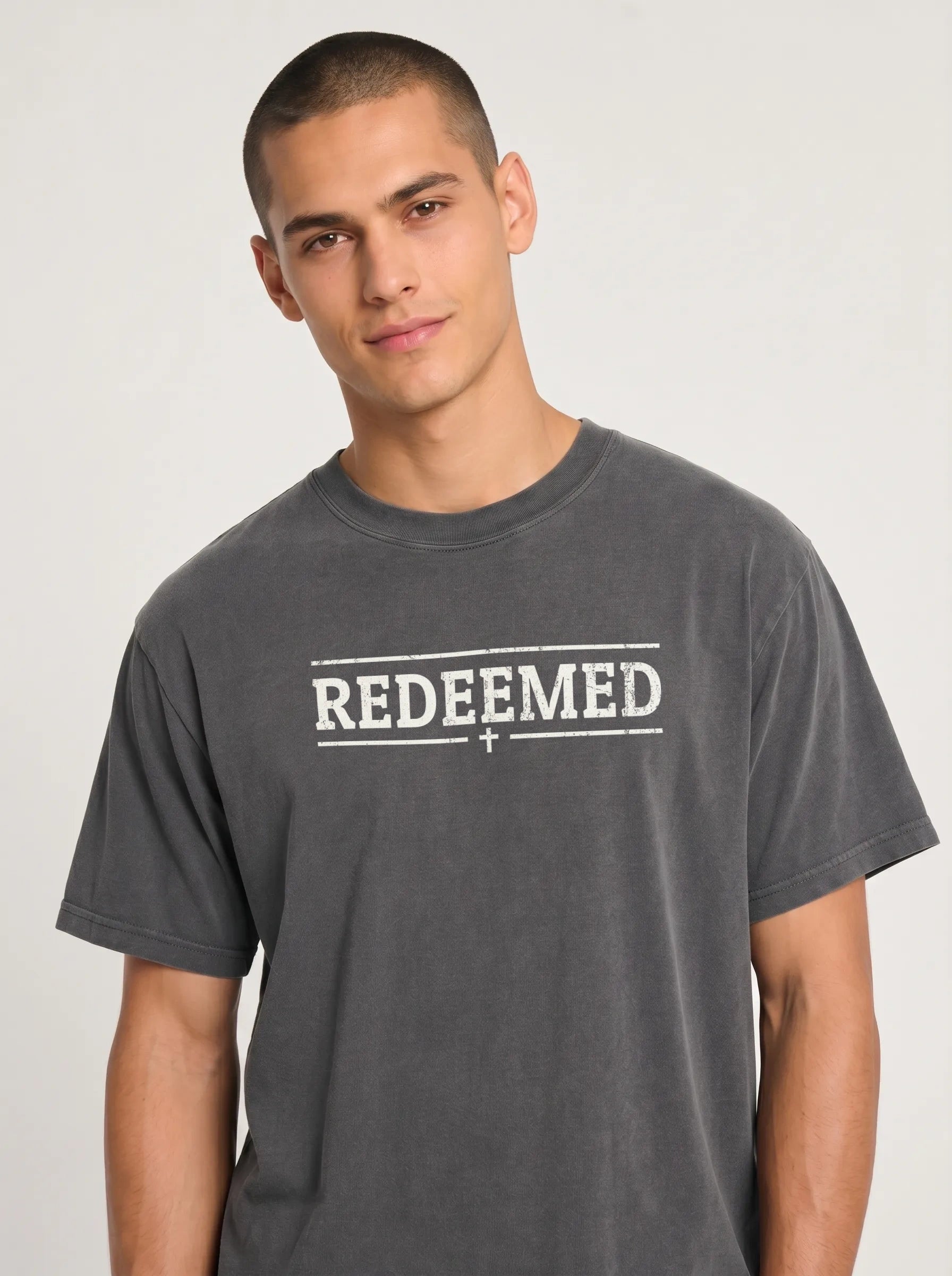 A man wearing a dark gray washed t-shirt with 'REDEEMED' printed in white across the chest, set against a plain light gray background.
