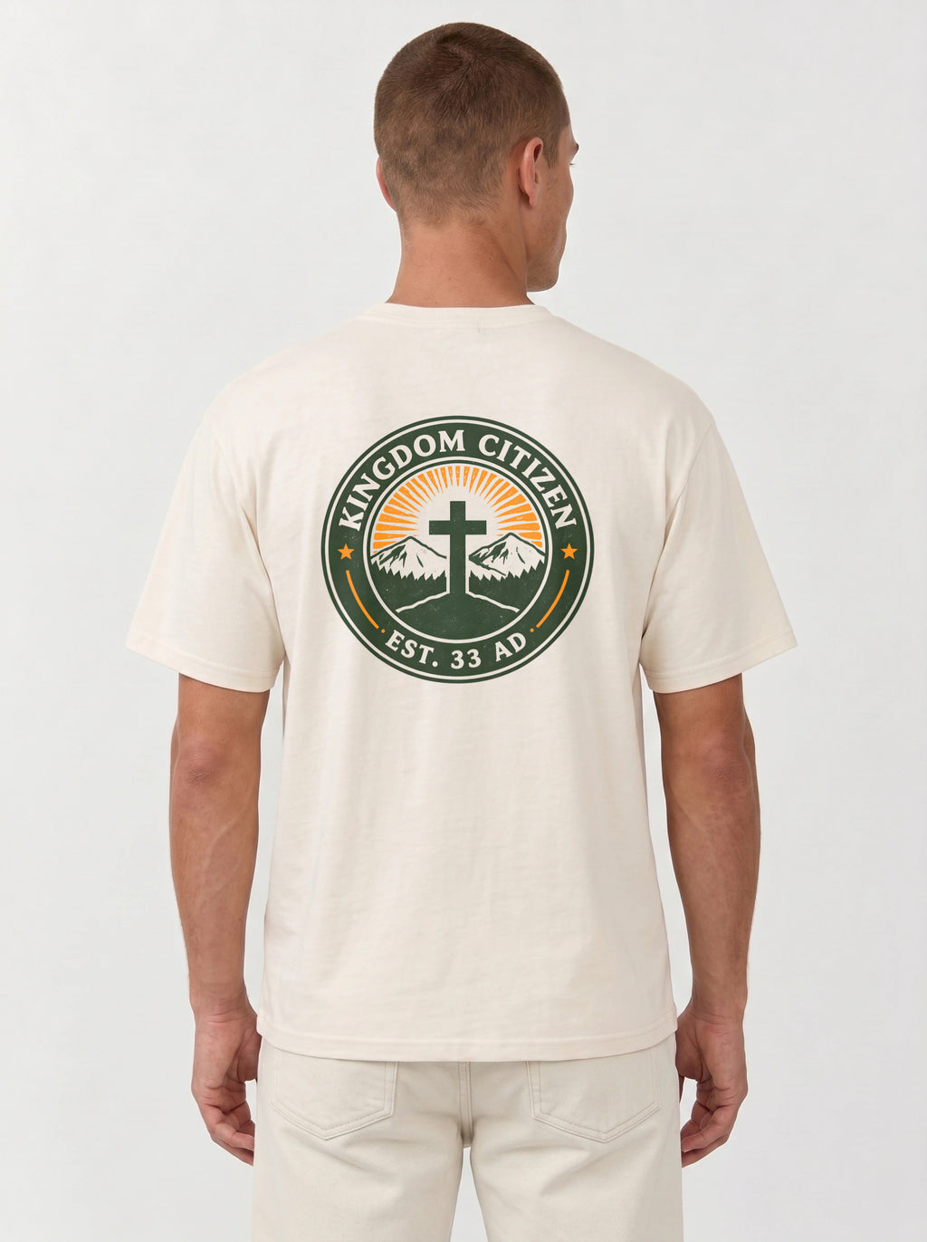 A man viewed from the back wearing a cream-colored t-shirt with a large circular graphic on the back. The graphic features a green border with the text 'KINGDOM CITIZEN' and 'EST. 33 AD.