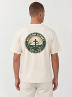 A man viewed from the back wearing a cream-colored t-shirt with a large circular graphic on the back. The graphic features a green border with the text 'KINGDOM CITIZEN' and 'EST. 33 AD.
