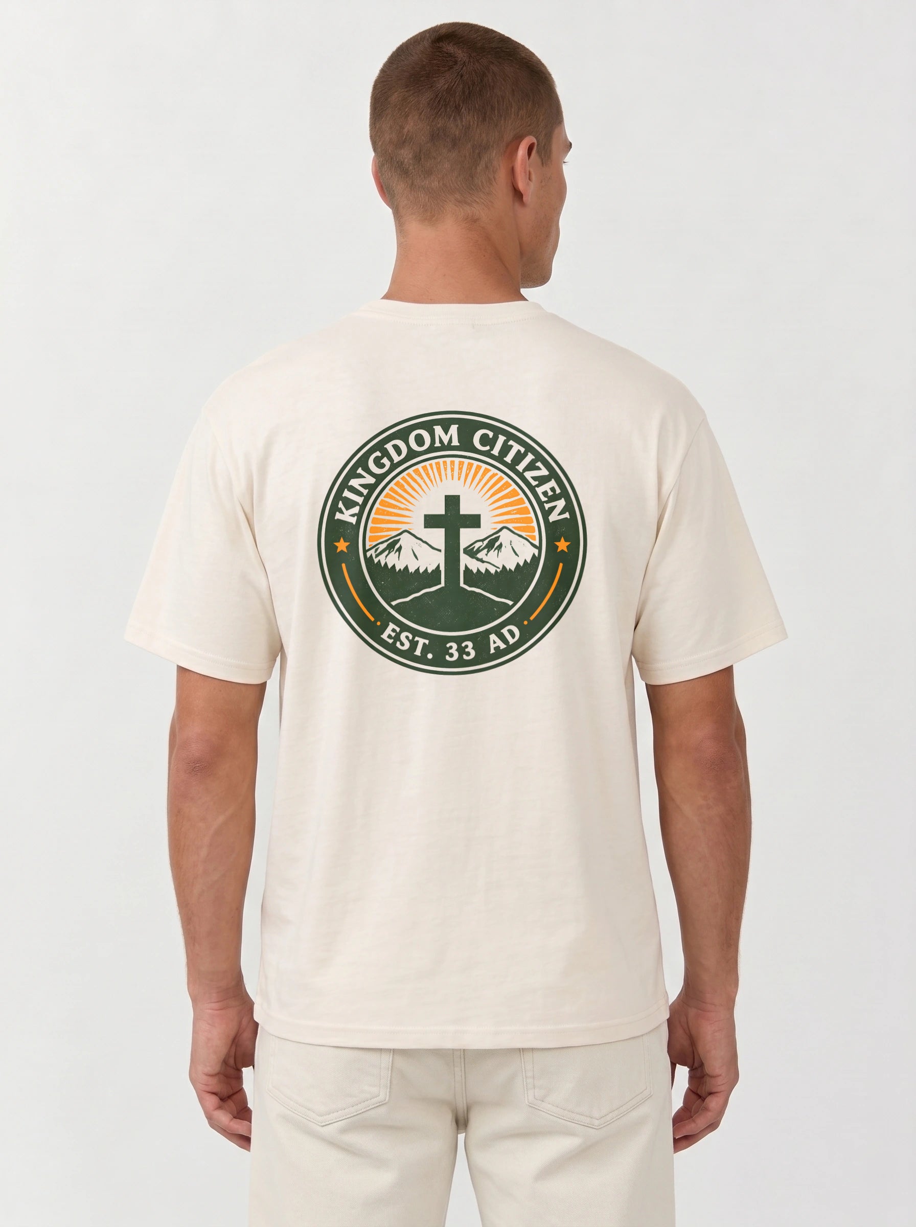 A man viewed from the back wearing a cream-colored t-shirt with a large circular graphic on the back. The graphic features a green border with the text 'KINGDOM CITIZEN' and 'EST. 33 AD.