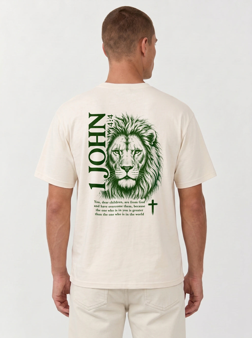 Person wearing a cream T-shirt with a green lion illustration, cross, “1 John 4:4,” and the verse text, “You, dear children, are from God and have overcome them, because the one who is in you is greater than the one who is in the world.”