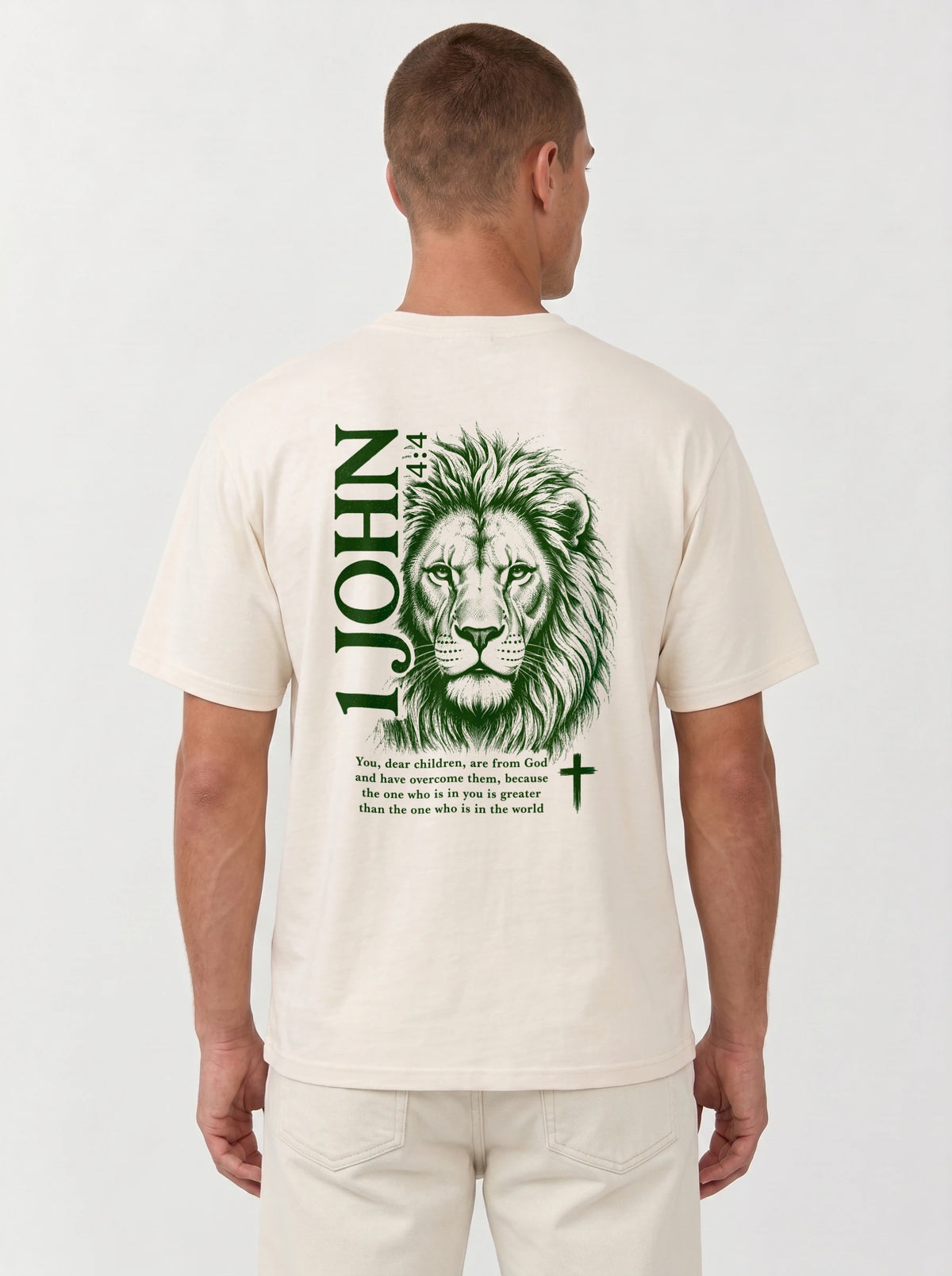 Person wearing a cream T-shirt with a green lion illustration, cross, “1 John 4:4,” and the verse text, “You, dear children, are from God and have overcome them, because the one who is in you is greater than the one who is in the world.”
