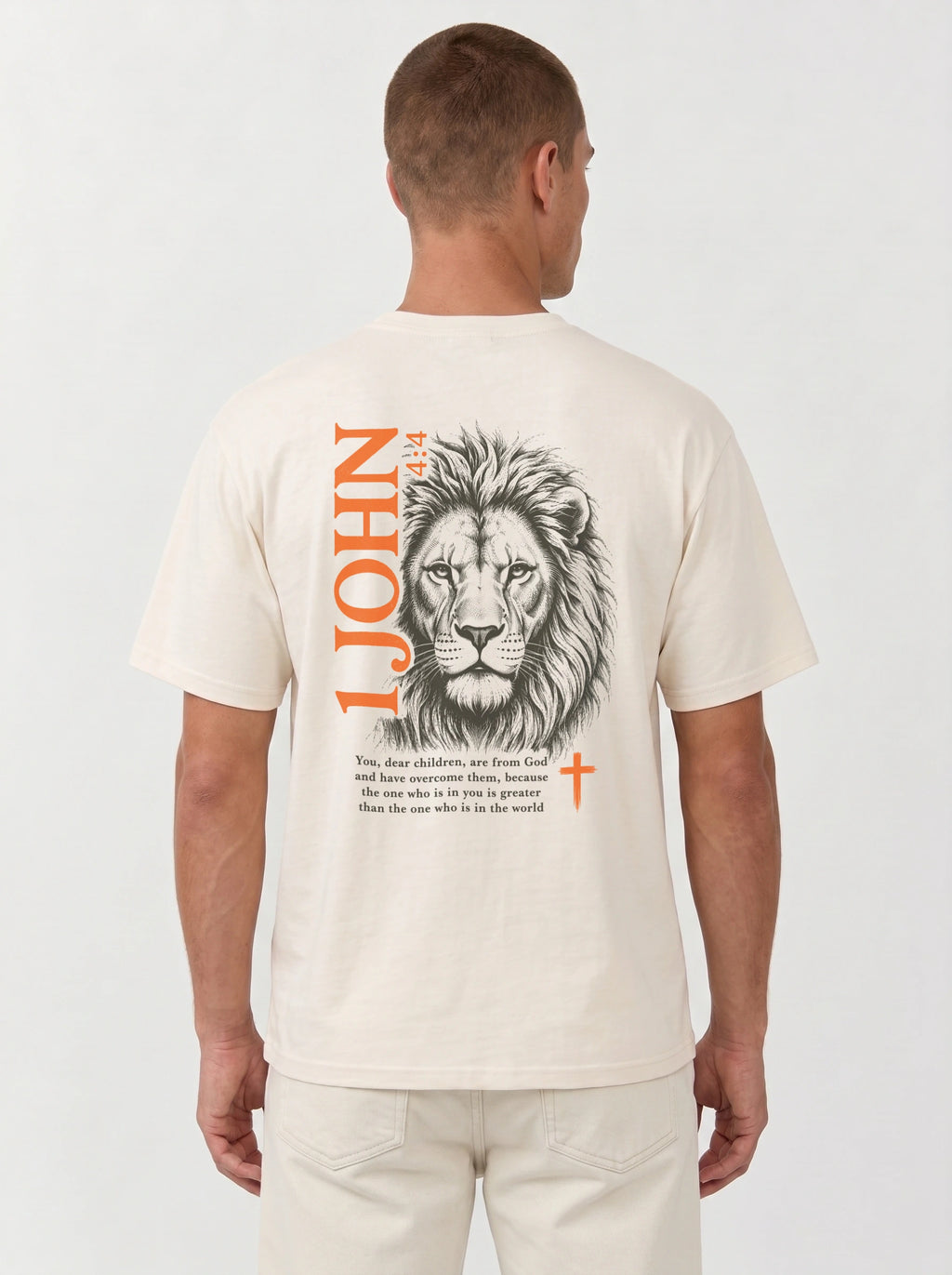 Person wearing a cream T-shirt with a lion illustration, orange “1 John 4:4” and cross, and the verse “You, dear children, are from God and have overcome them, because the one who is in you is greater than the one who is in the world.”