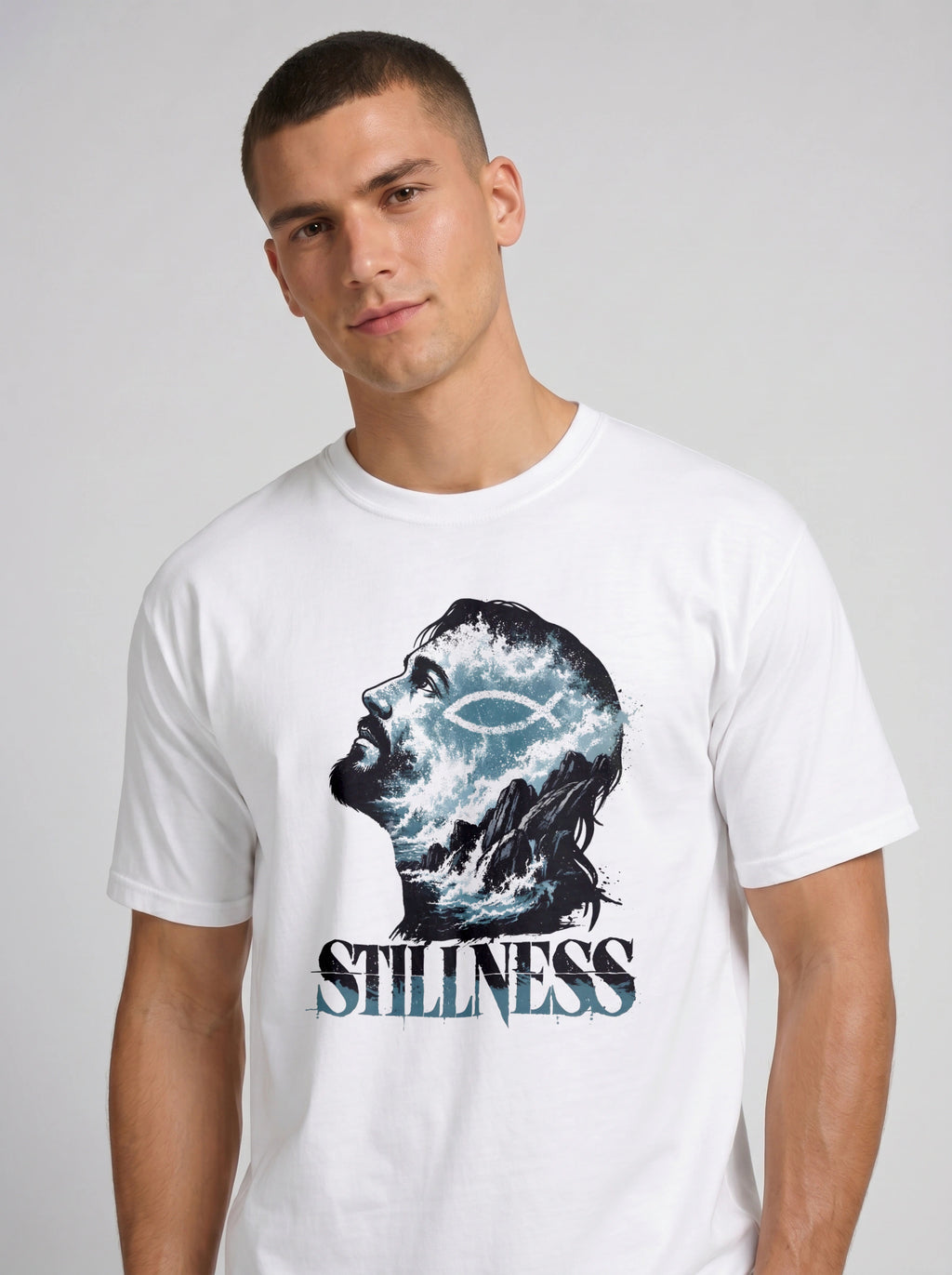 A man wearing a white crewneck t-shirt with a graphic print of a profile head filled with stormy blue and white clouds, featuring the word 'STILLNESS' in a stylized font below it.