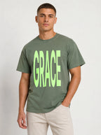 Person wearing a muted green T-shirt with large neon green text reading “GRACE.”