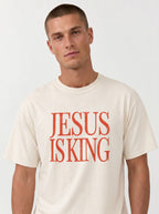 Person wearing a cream T-shirt with distressed orange text reading “Jesus Is King.”