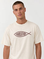 A man wearing a cream-colored t-shirt with a dark brown graphic of a fish containing the text 'FISHERS OF MEN' on the chest, set against a plain light gray background.