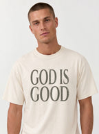 Person wearing a cream T-shirt with distressed gray text reading “God is Good.”