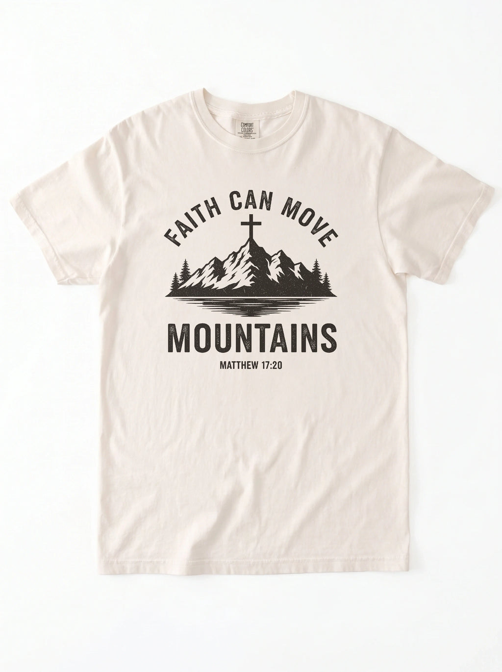 An off-white crewneck t-shirt with a black graphic print on the front. The graphic features a mountain silhouette with a cross on top, the text 'FAITH CAN MOVE MOUNTAINS', and 'MATTHEW 17:20' underneath.