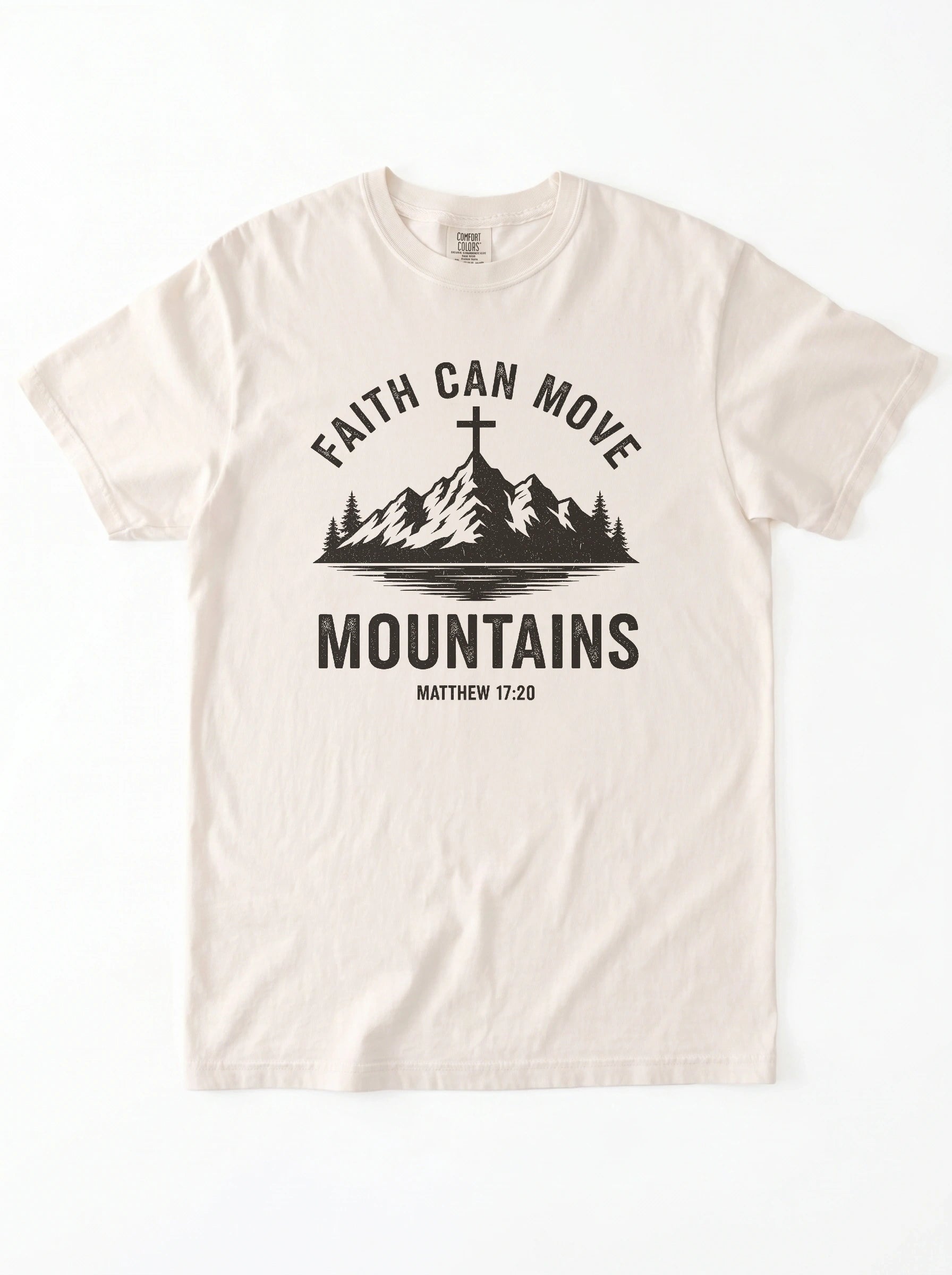 An off-white crewneck t-shirt with a black graphic print on the front. The graphic features a mountain silhouette with a cross on top, the text 'FAITH CAN MOVE MOUNTAINS', and 'MATTHEW 17:20' underneath.