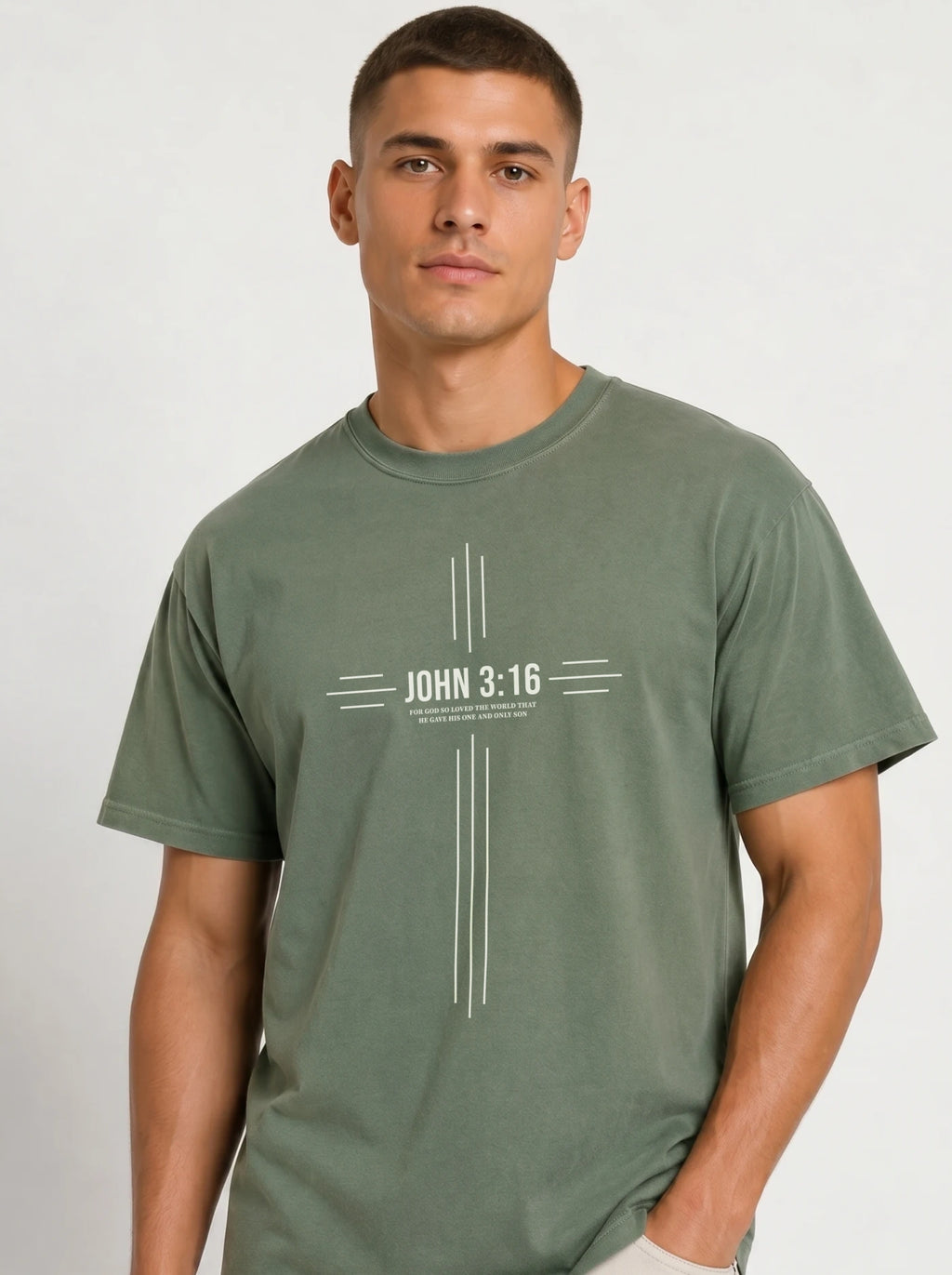 Person wearing a muted green T-shirt with a white cross-shaped design reading “John 3:16” and “For God so loved the world that he gave his one and only son.”