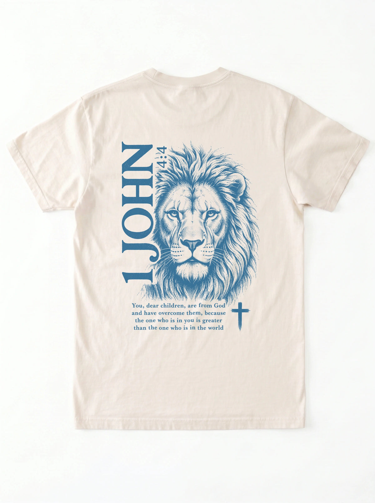 Flat lay of a cream-colored garment-dyed t-shirt, back view, laid on a white surface. It shows a large blue lion illustration with '1 JOHN 4:4' text, a Bible verse, and a small cross symbol.