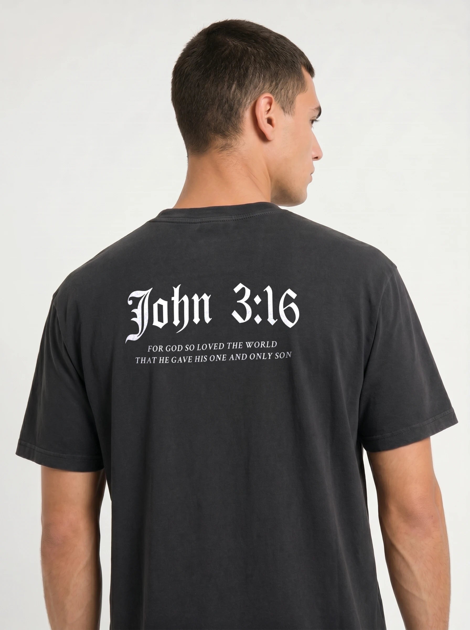 A man shown from the back wearing a black t-shirt with white gothic-style text reading 'John 3:16' and a Bible verse underneath.