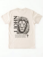 Cream T-shirt laid flat with black “1 John 4:4” text and a cross printed on the chest.