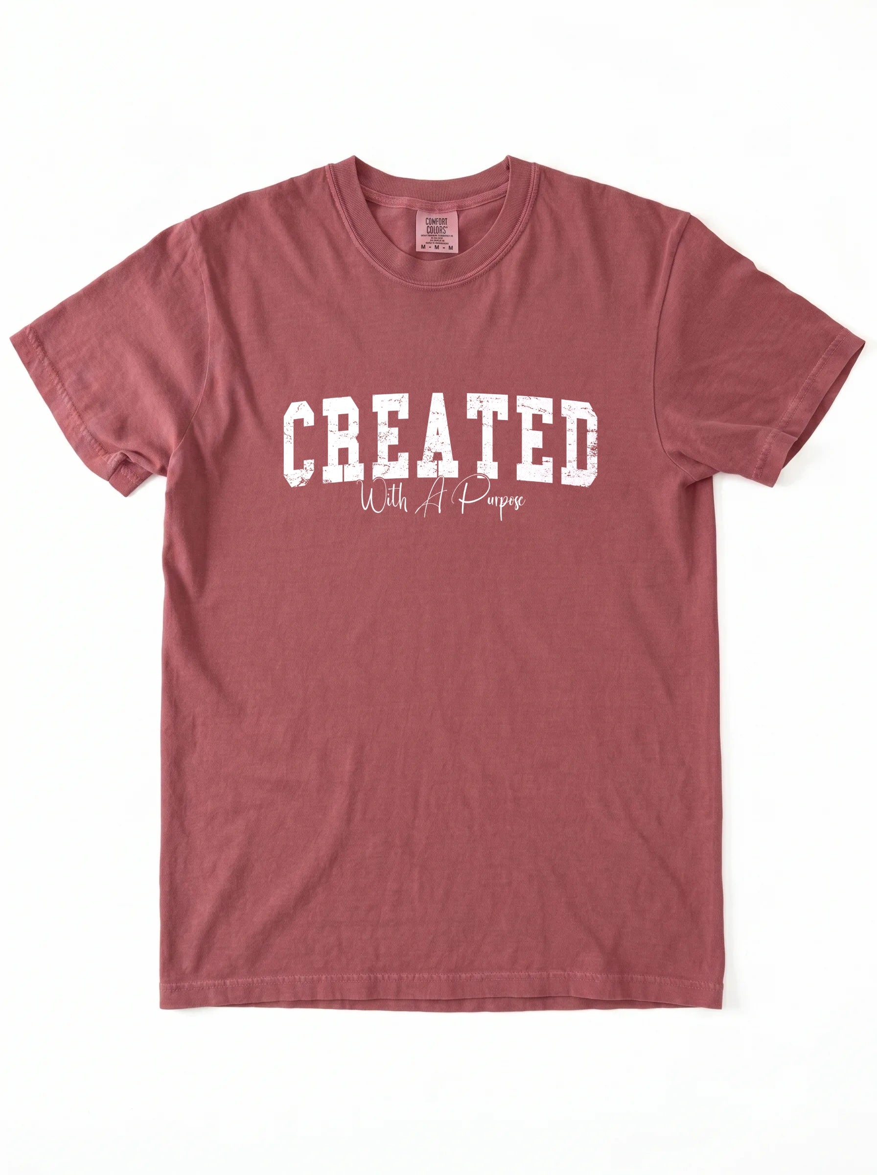A dusty rose short-sleeve t-shirt with 'CREATED With A Purpose' printed in white on the front, laid flat against a white background.