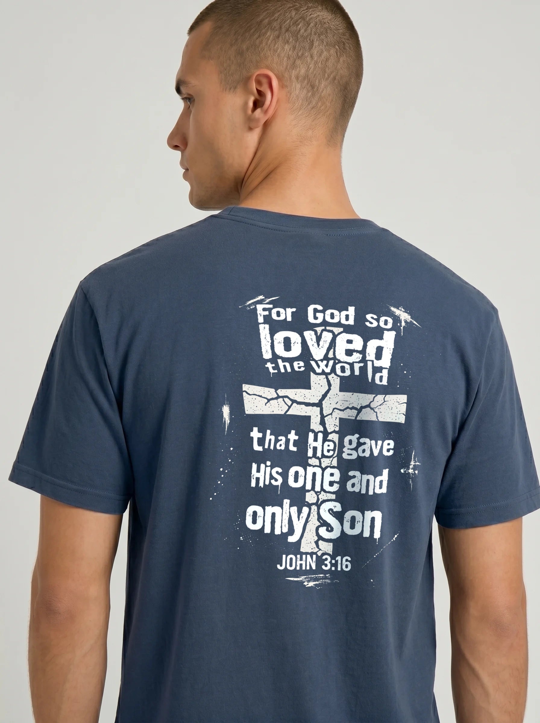 A man wearing a navy blue t-shirt, viewed from the back. The shirt features a large white graphic print with a cross and the biblical quote 'For God so loved the world that He gave His one and only Son JOHN 3:16'.