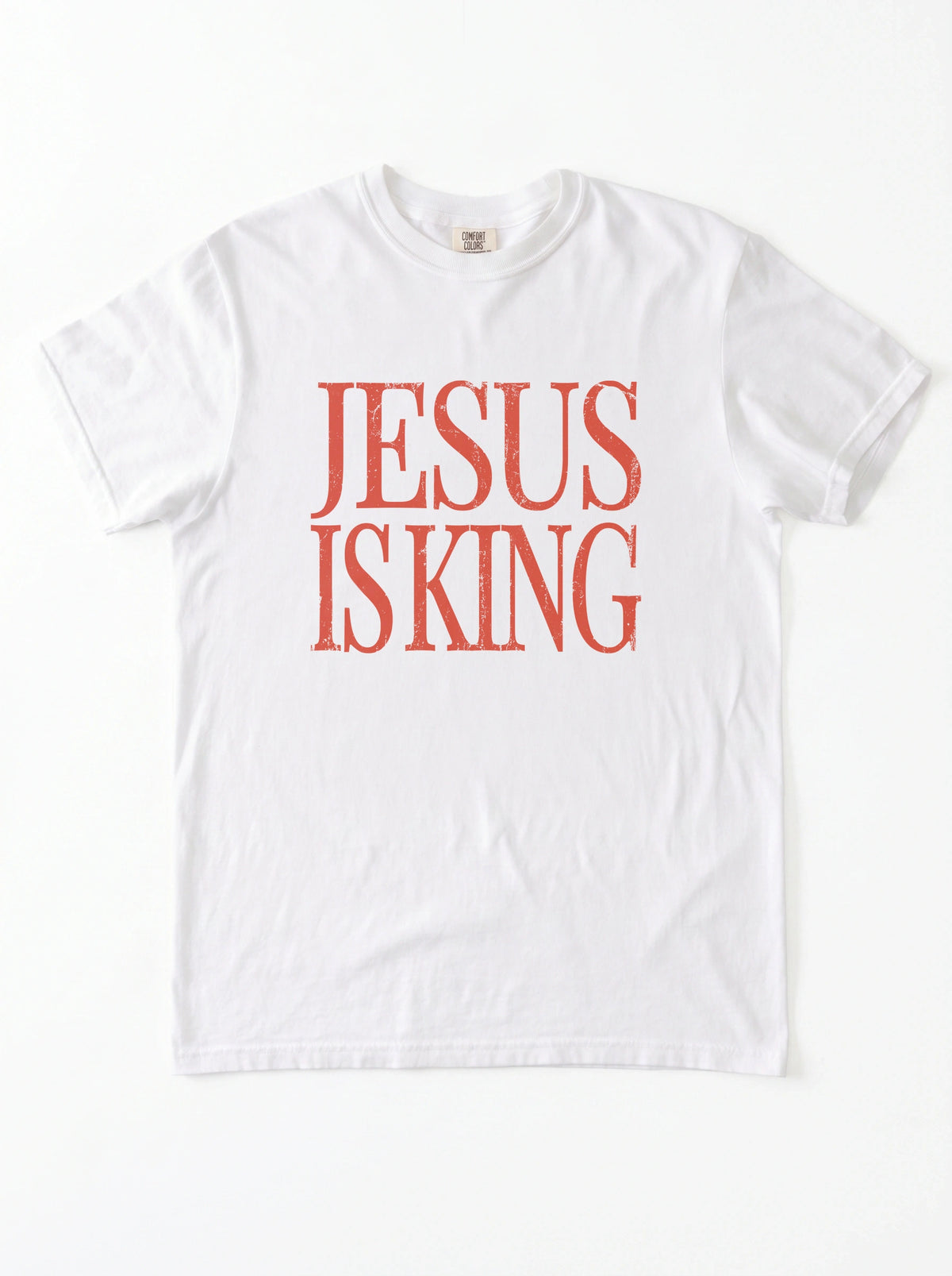White T-shirt laid flat with distressed orange text reading “Jesus Is King.”