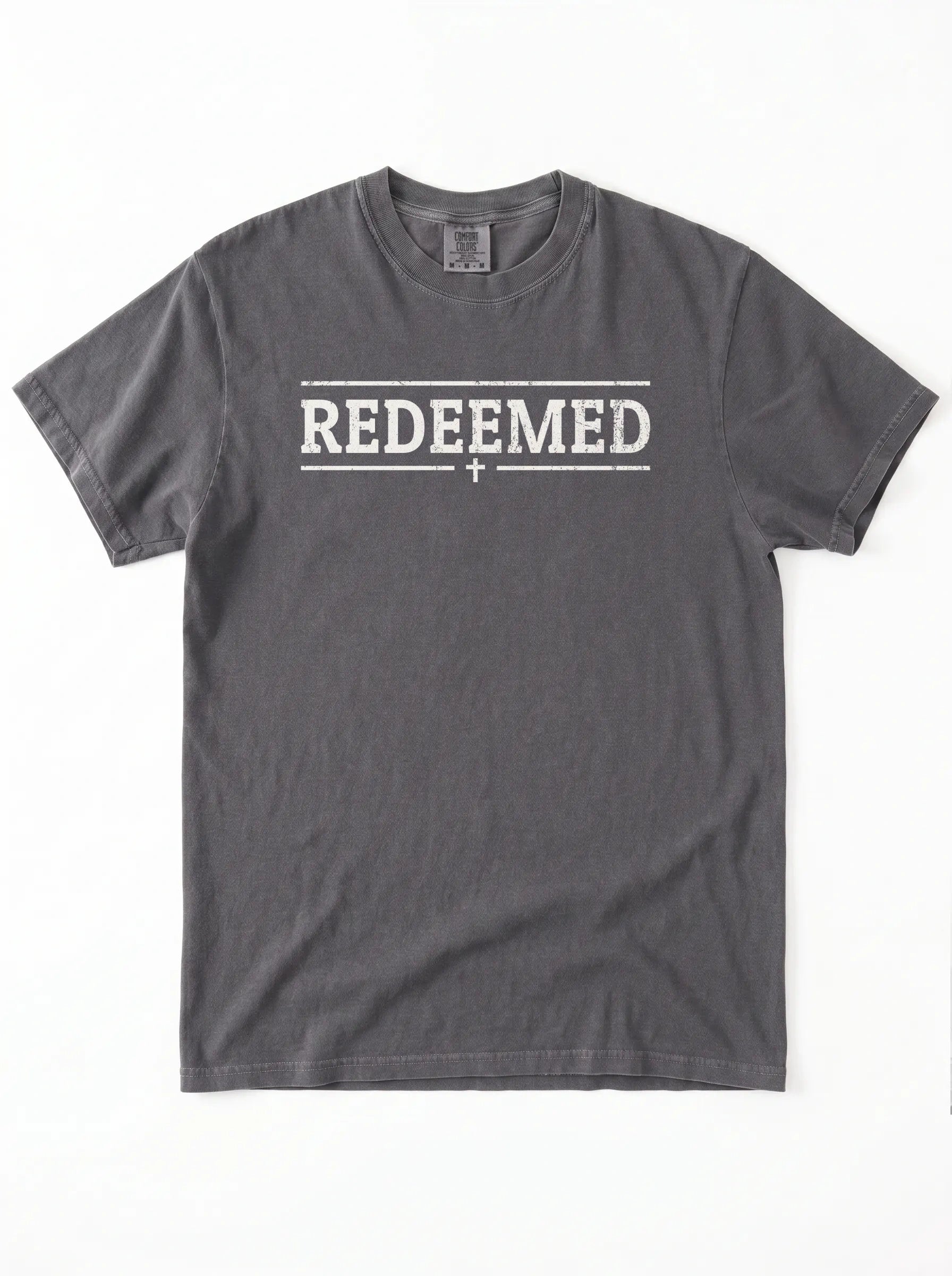 A dark gray crewneck t-shirt with 'REDEEMED' printed in distressed white block letters across the chest, flanked by two horizontal lines and a small cross below, shown flat on a white background.