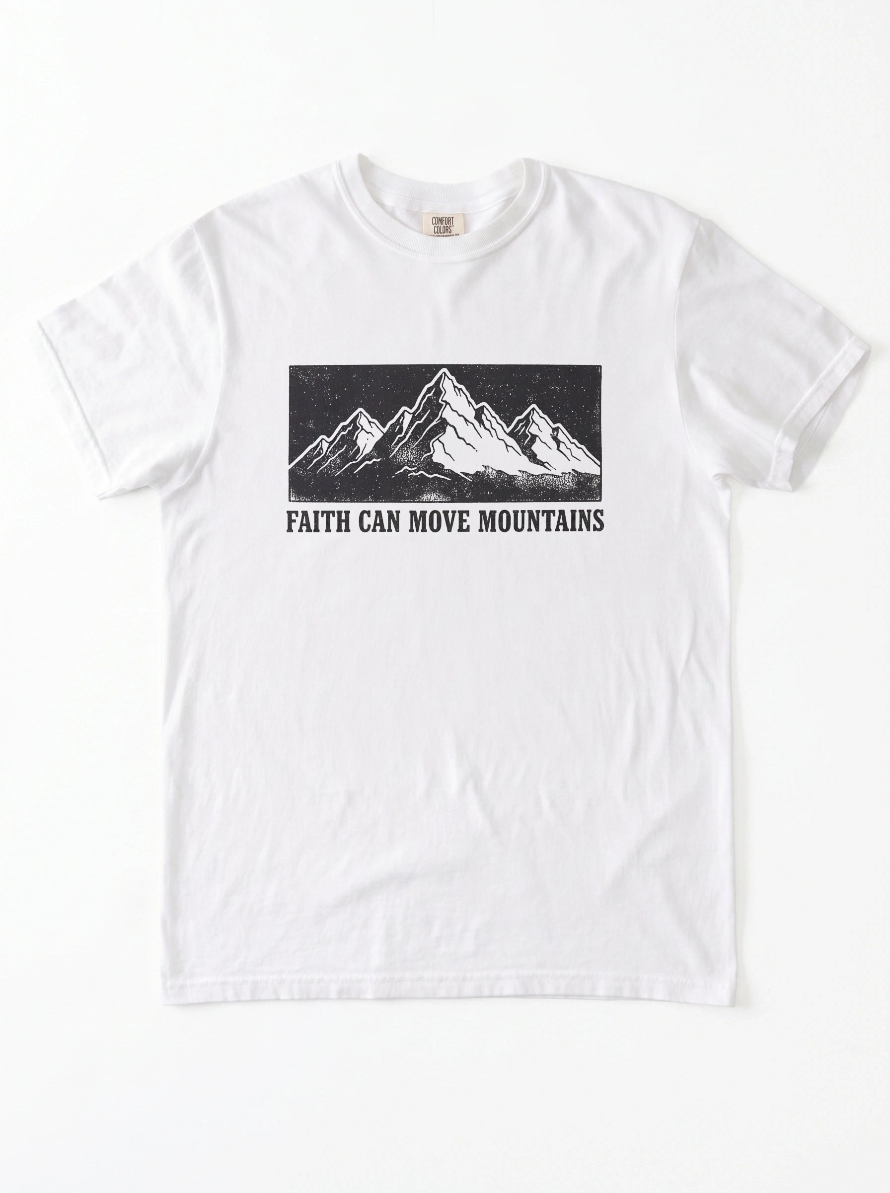 A white short-sleeve crewneck t-shirt featuring a black graphic of a mountain range and the text 'FAITH CAN MOVE MOUNTAINS' printed on the chest.