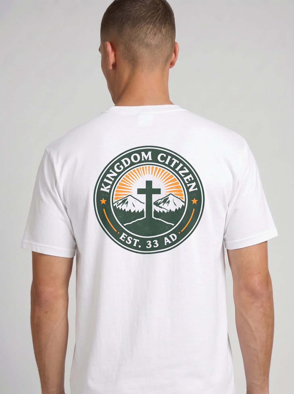 A man viewed from the back wearing a white t-shirt with a large circular graphic on the back. The graphic features a green border with the text 'KINGDOM CITIZEN' and 'EST. 33 AD.