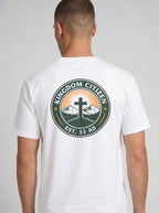 A man viewed from the back wearing a white t-shirt with a large circular graphic on the back. The graphic features a green border with the text 'KINGDOM CITIZEN' and 'EST. 33 AD.
