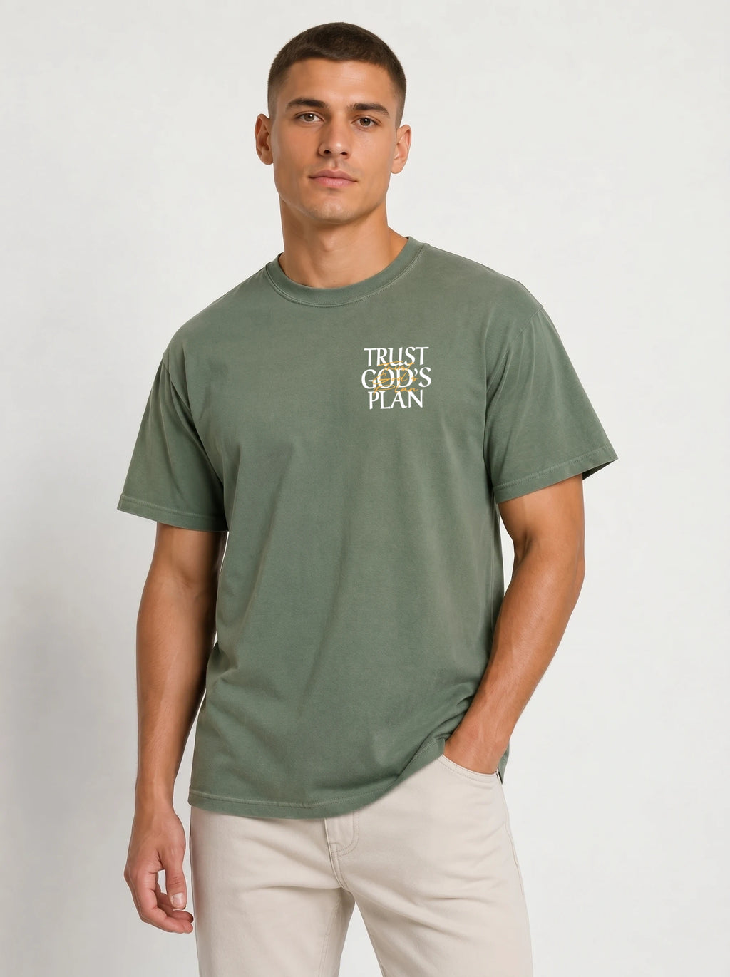 Person wearing a muted green T-shirt with a small chest design reading “TRUST GOD’S PLAN.”