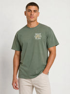 Person wearing a muted green T-shirt with a small chest design reading “TRUST GOD’S PLAN.”