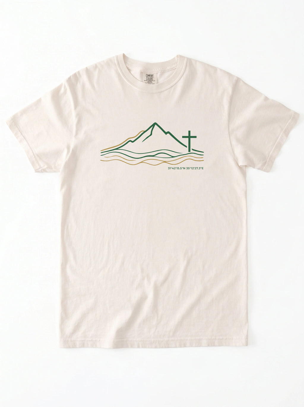 An off-white crewneck t-shirt featuring a graphic of a minimalist line art logo featuring a mountain range above flowing river lines, with a Christian cross standing on the right side. The design is drawn in green and gold on a light background, with geographic coordinates printed beneath the landscape.