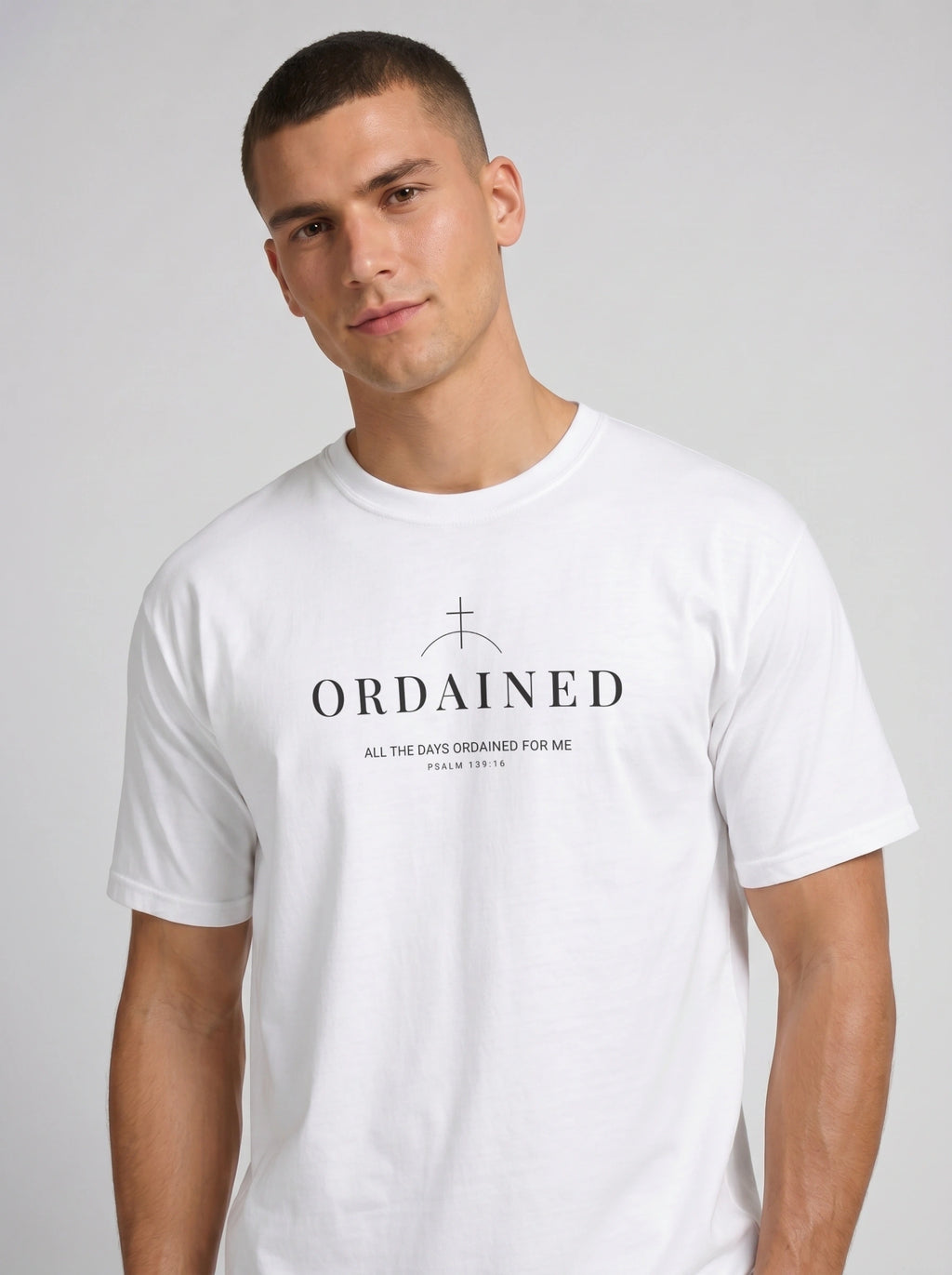 A man wearing a white crew-neck t-shirt with the word 'ORDAINED' and 'ALL THE DAYS ORDAINED FOR ME', set against a plain light gray background.