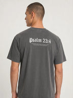 A man viewed from the back wearing a dark gray washed t-shirt with 'Psalm 23:4' printed in white Gothic lettering across the upper back.