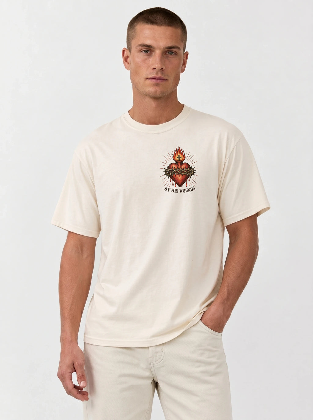 Cream T-shirt with a flaming sacred heart wrapped in a crown of thorns and the text “By His Wounds.”