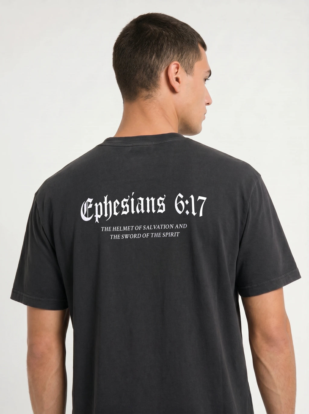 A man viewed from the back wearing a dark charcoal gray t-shirt with white gothic text reading 'Ephesians 6:17' and smaller scripture text underneath.