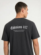 A man viewed from the back wearing a dark charcoal gray t-shirt with white gothic text reading 'Ephesians 6:17' and smaller scripture text underneath.