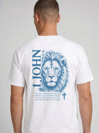 A man wearing a white garment-dyed t-shirt, viewed from the back. The shirt features a large blue lion illustration with '1 JOHN 4:4' text, a Bible verse, and a small cross symbol.