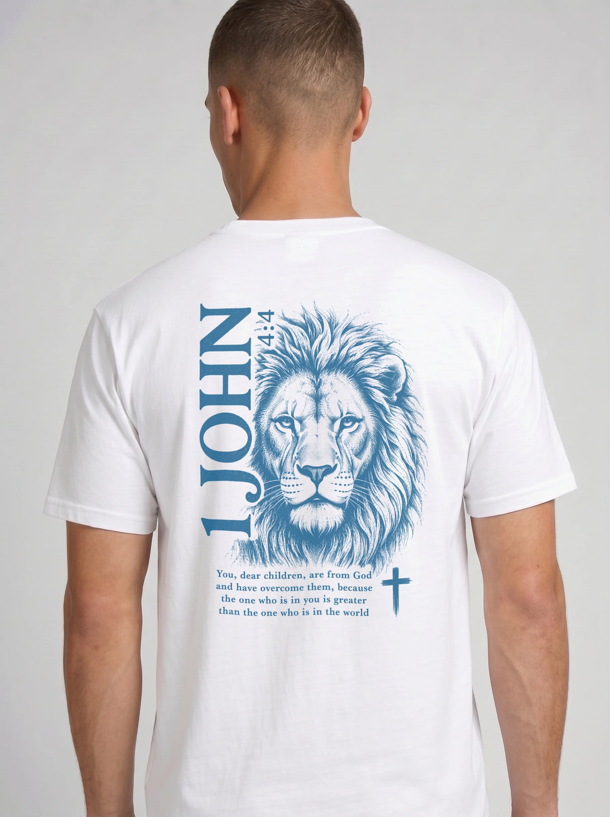 A man wearing a white garment-dyed t-shirt, viewed from the back. The shirt features a large blue lion illustration with '1 JOHN 4:4' text, a Bible verse, and a small cross symbol.