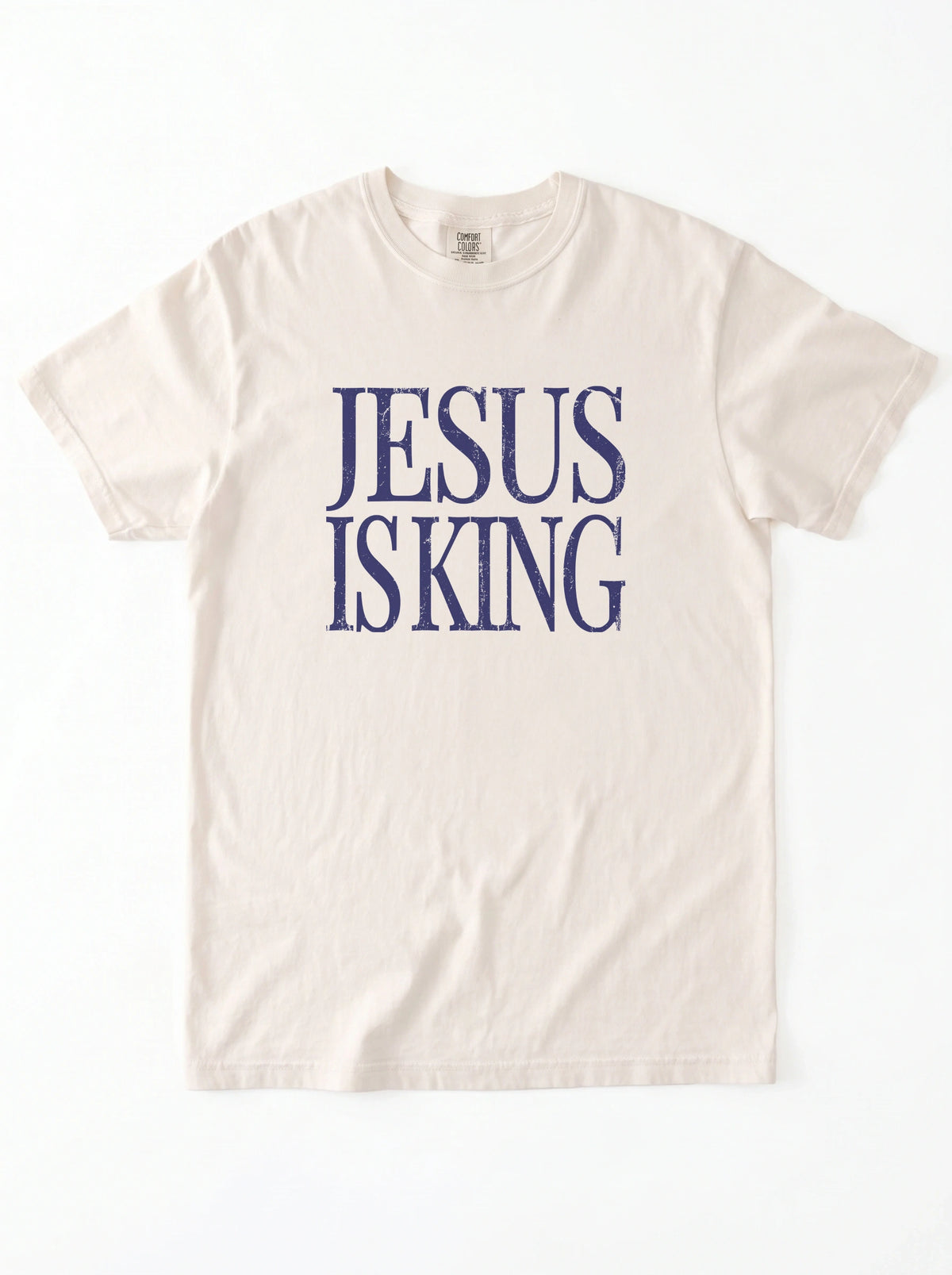 Cream T-shirt laid flat with distressed navy text reading “Jesus Is King.”