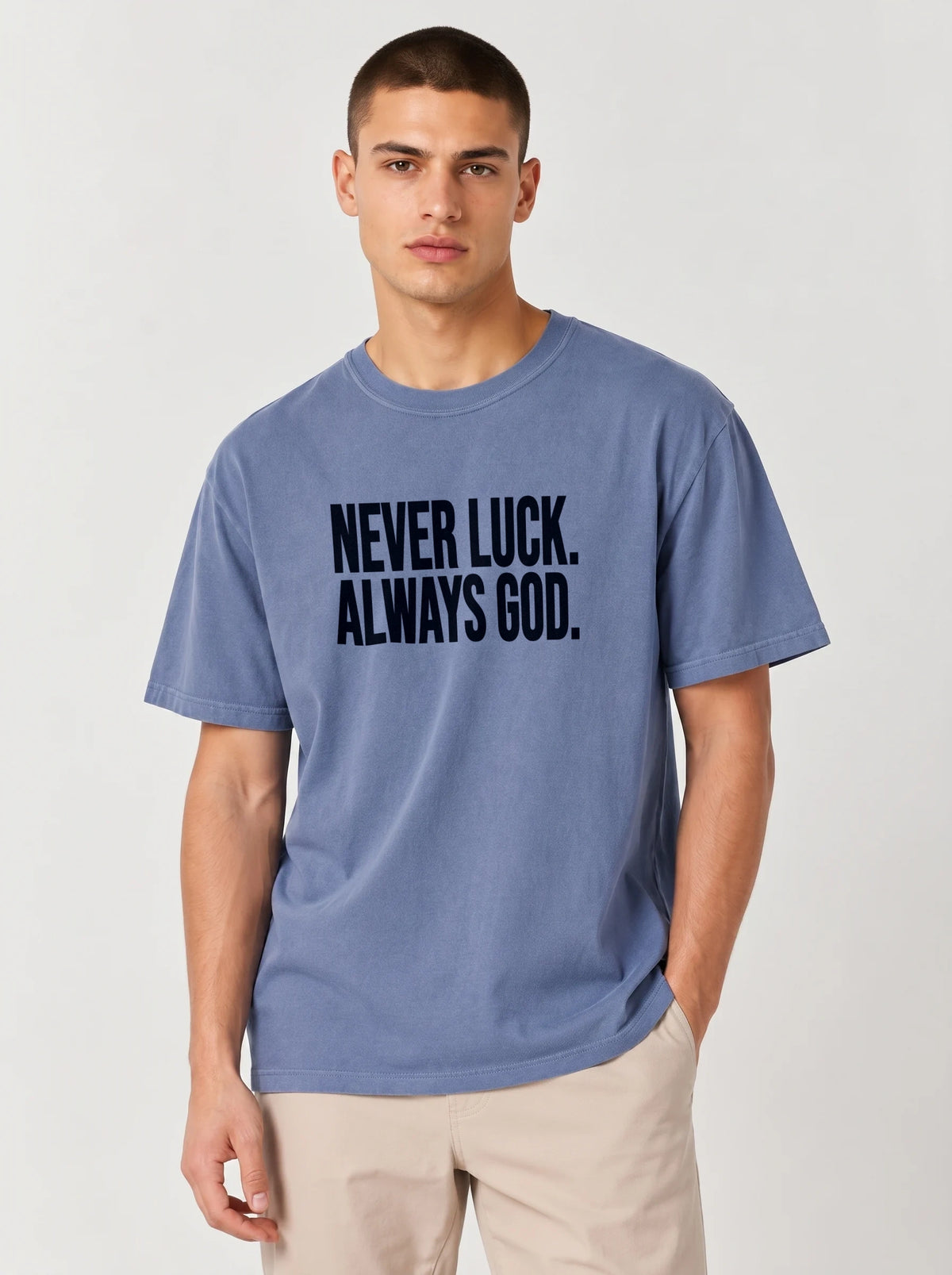 Person wearing a faded blue T-shirt with dark text reading “Never luck. Always God.”