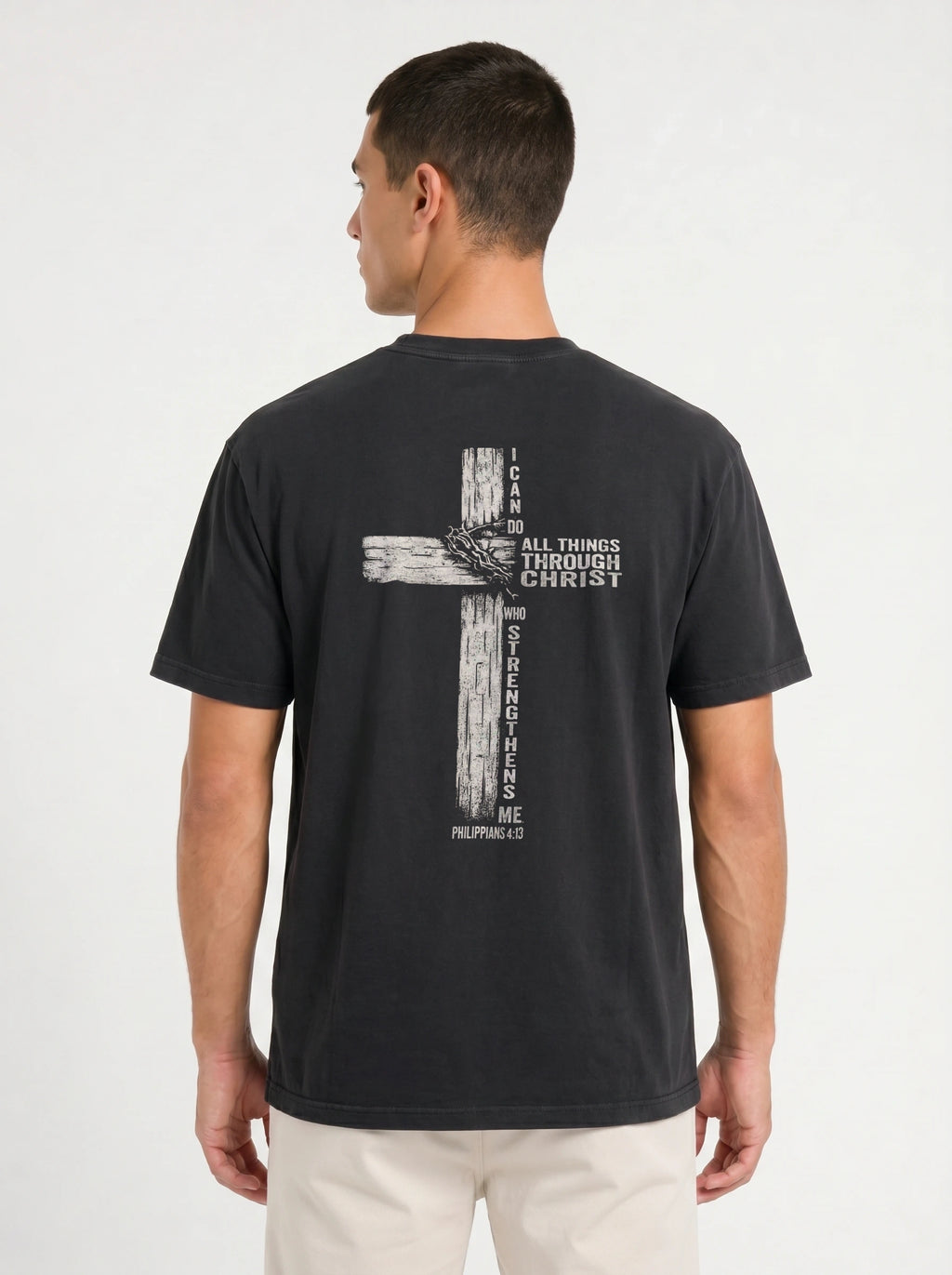 A man wearing a faded black t-shirt from the back, featuring a distressed biege graphic of a cross with the text 'I CAN DO ALL THINGS THROUGH CHRIST WHO STRENGTHENS ME' from Philippians 4:13.