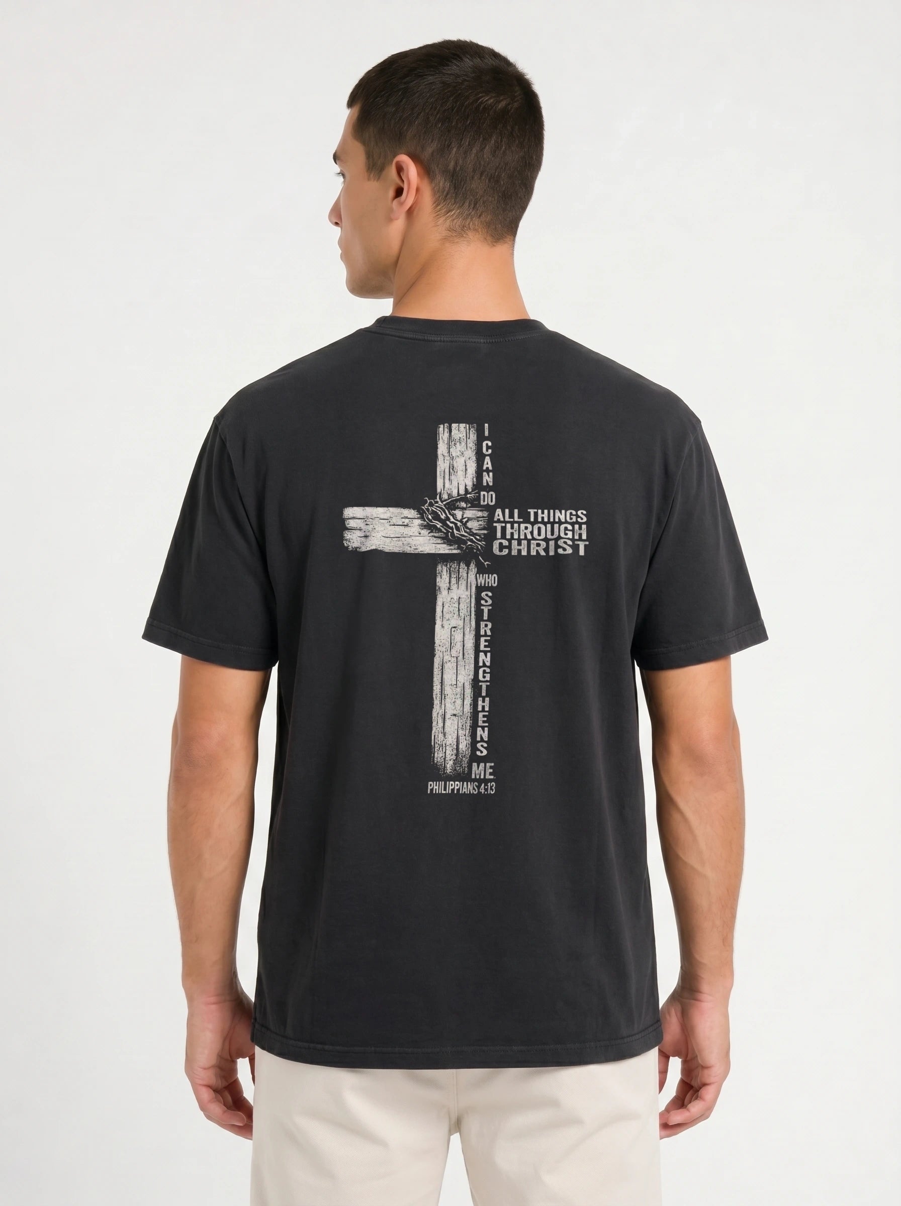 A man wearing a faded black t-shirt from the back, featuring a distressed biege graphic of a cross with the text 'I CAN DO ALL THINGS THROUGH CHRIST WHO STRENGTHENS ME' from Philippians 4:13.