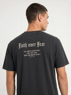 A man shown from the back wearing a dark charcoal gray t-shirt with a white gothic-style text graphic reading 'Faith over Fear' and a bible verse on the back.