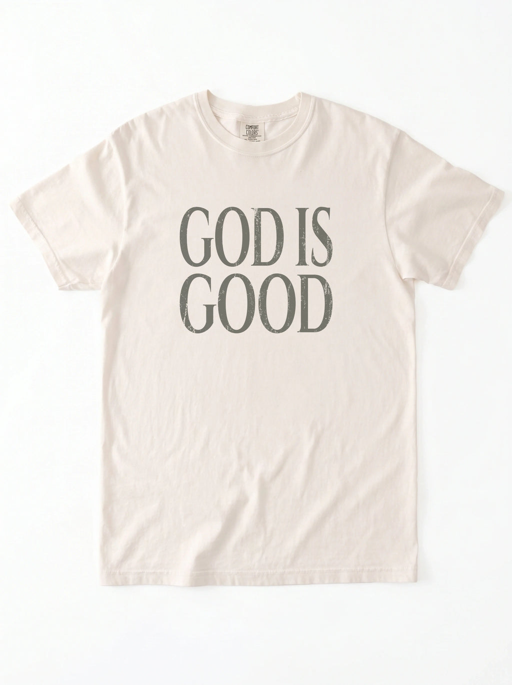 Cream T-shirt laid flat with distressed gray text reading “God is Good.”