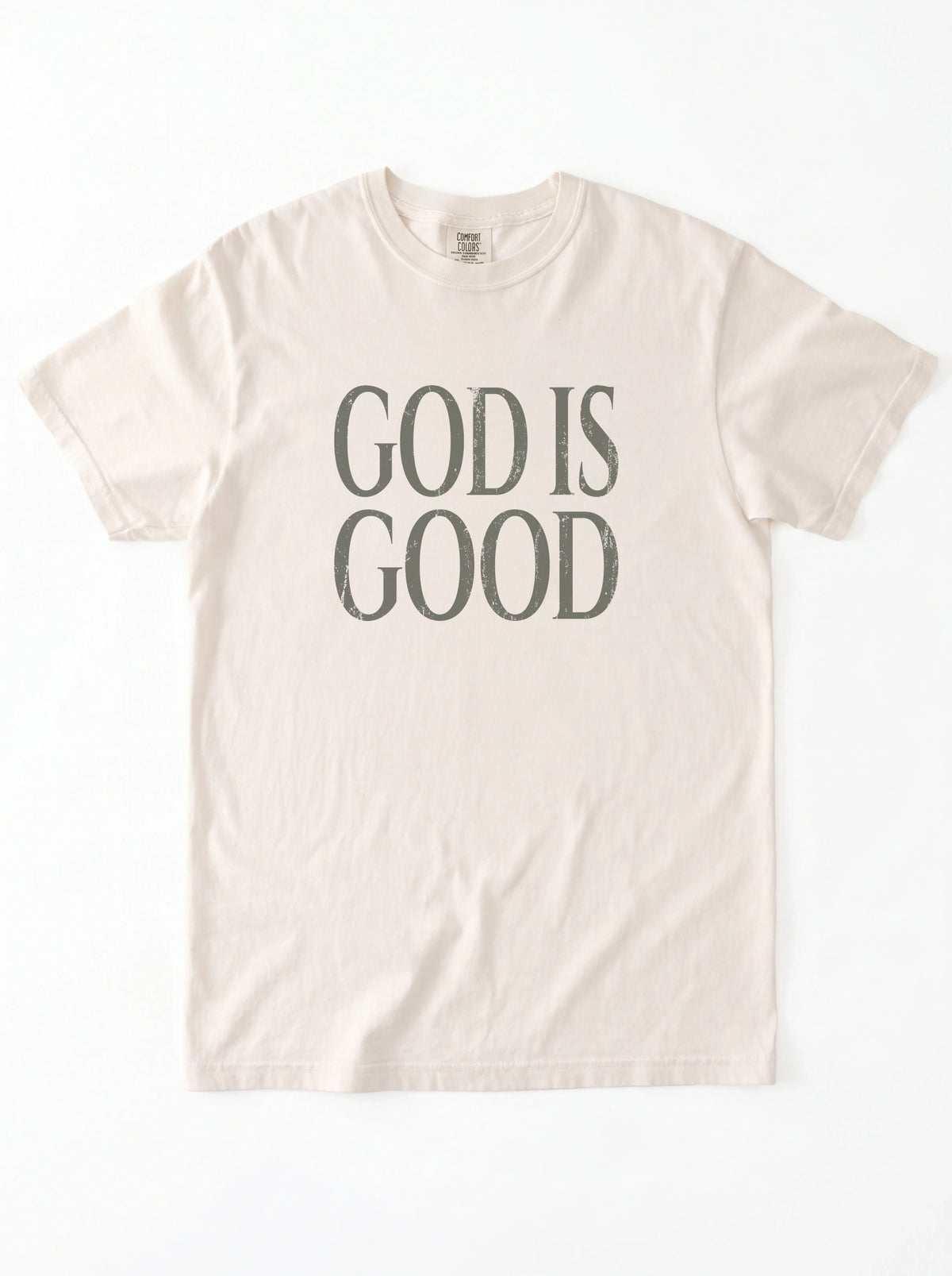 Cream T-shirt laid flat with distressed gray text reading “God is Good.”