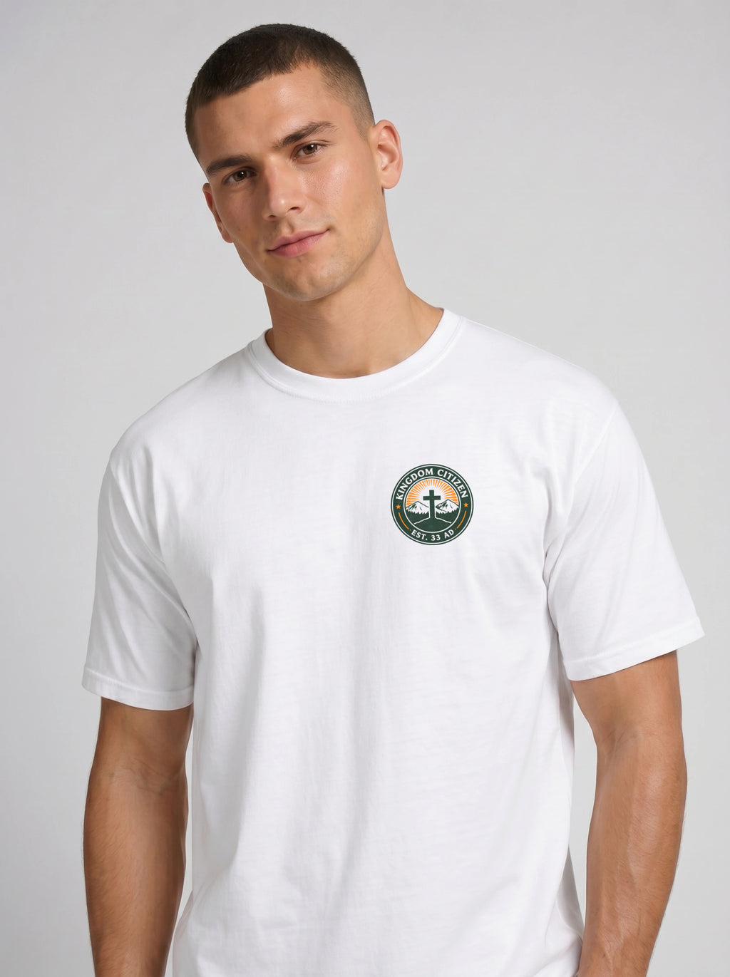 A man wearing a white short-sleeve crewneck t-shirt with a circular graphic on the left side of chest. The graphic features a green border with the text 'KINGDOM CITIZEN' and 'EST. 33 AD.