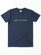 A navy blue short-sleeve t-shirt with the phrase 'GOD IS GOOD' printed in white across the chest, with a small white cross symbol underneath, laid flat against a white background.