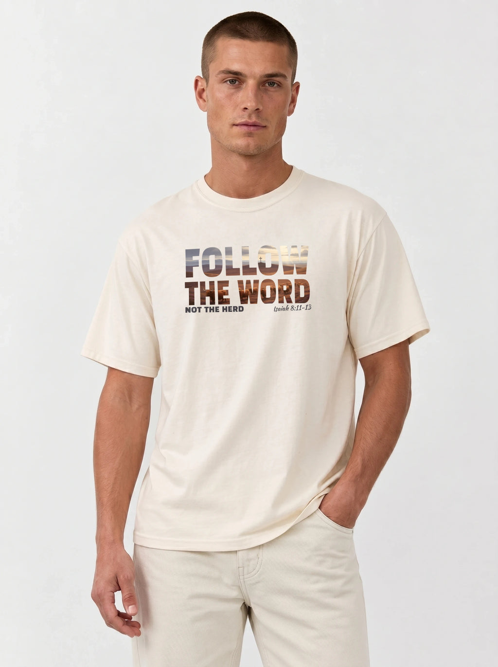 A man wearing a cream-colored t-shirt with a graphic that reads 'FOLLOW THE WORD NOT THE HERD' and 'Isaiah 8:11-13' in a textured, multi-toned font, paired with light beige pants, against a plain light gray background.