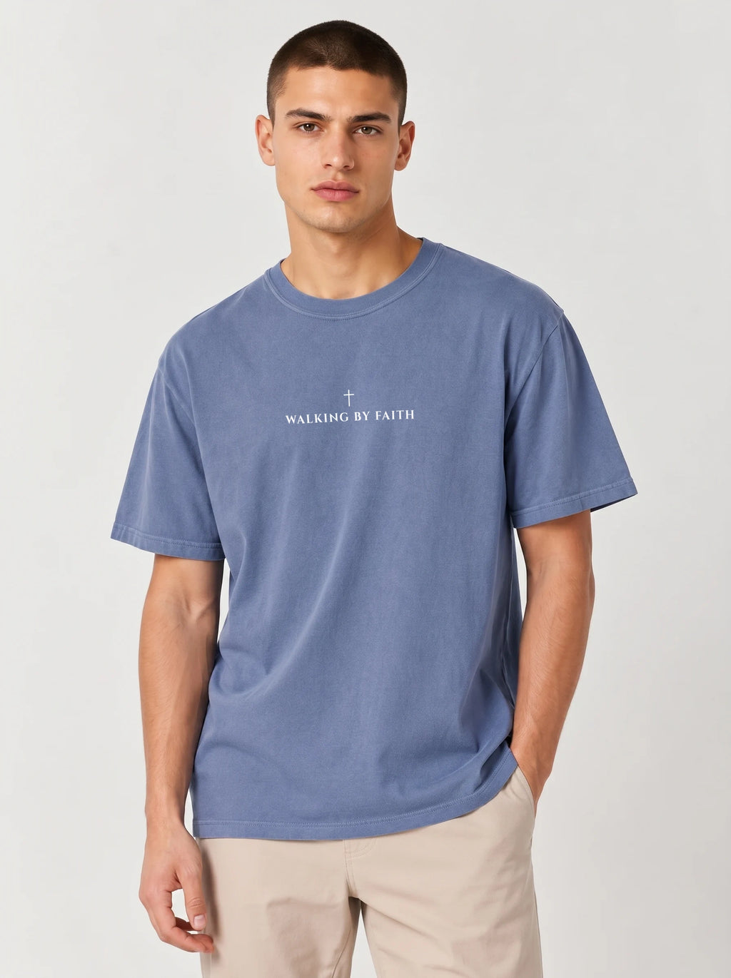 A man wearing a faded blue crewneck t-shirt with a white graphic print on the chest that reads 'Walking By Faith'.